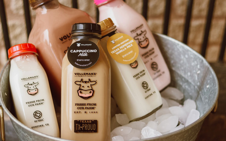 5 glass bottles showcasing different flavors of milk sitting in a bucket chilling on ice.